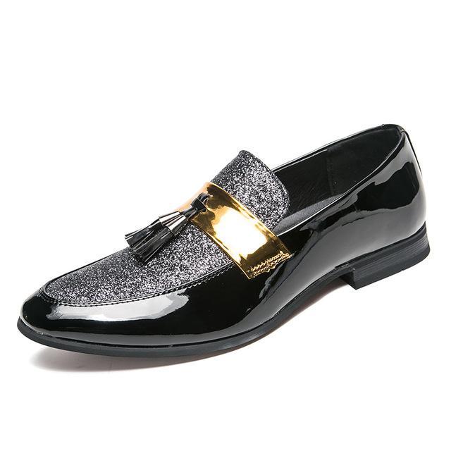 Men's black shiny flat shoes with tassel detail and gold accent.